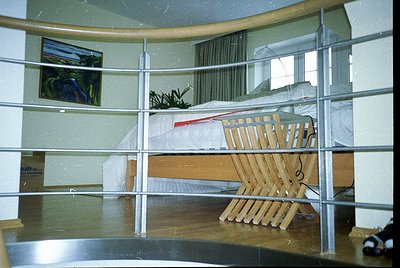 Mid-century modern hotel room with curved balcony railing. Wooden lounge chair and ottoman positioned outside, overlooking a ...
