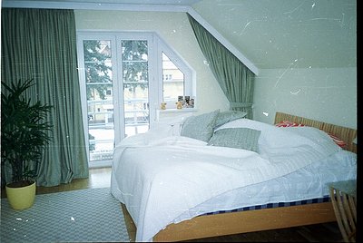 Spacious alpine-style bedroom with sloped ceiling, large double bed in neutral tones, and floor-to-ceiling sliding glass door...