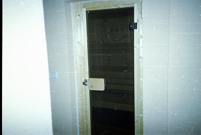 Vintage institutional door with wooden plank interior and metal latch, set in white-tiled corridor. Likely mid-20th century i...