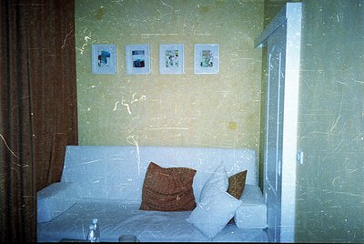 Vintage hotel room with mid-century design—marble-walled corridor leading to a sofa bed in muted tones, framed photos depicti...