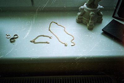 Vintage gold-toned jewelry—ring, bracelet, and necklace—scattered on a worn marble surface beside a classical stone pedestal....