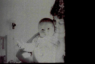Vintage sepia-toned indoor portrait of an infant in a high chair, holding a toy. Blurred background reveals a simple room wit...