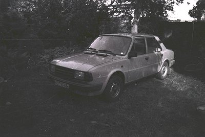 Vintage hatchback sedan parked on uneven grass beside a stone wall, likely a Škoda from the 1970s–1980s. Distinctive boxy des...