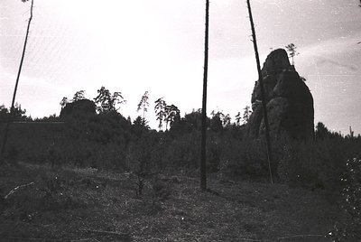 Vintage black-and-white shot of rugged alpine terrain with striking rock formations and sparse forest. Overgrown trail and ut...