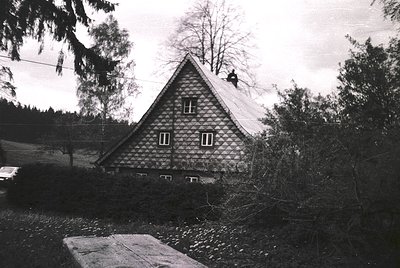 A black-and-white photo of a traditional alpine chalet with diamond-patterned wooden siding, steep gabled roof, and small rec...