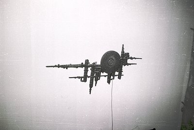 Vintage industrial silhouette of a mechanical arm with a circular wheel attachment, mounted on a plain wall. Likely a 20th-ce...