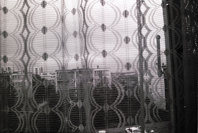 Distorted urban reflection through patterned glass, likely industrial or decorative. Symmetrical circular motifs create abstr...