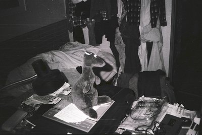 Cluttered 1960s-era workspace with vintage desk setup: typewriter, stack of papers, and framed photo. Darkroom-style lighting...