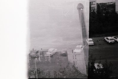 Vintage black-and-white shot of a coastal industrial site with a tall, cylindrical cooling tower and low-rise buildings. Fog ...
