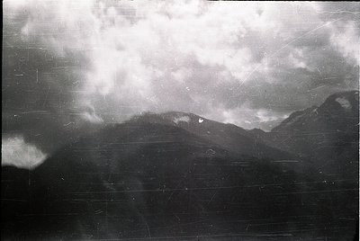 Vintage black-and-white shot of a dramatic storm front over mountainous terrain, likely captured mid-20th century. Low-hangin...