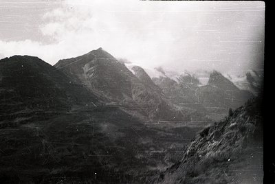 Vintage black-and-white alpine landscape with jagged peaks shrouded in mist, suggesting early 20th-century photography. Foreg...