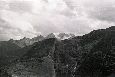 Vintage black-and-white aerial shot of rugged alpine peaks with jagged ridges, likely from the 20th century. Snow-capped summ...