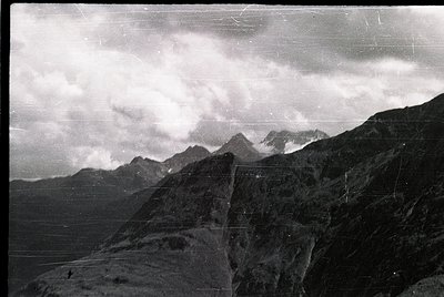 Vintage black-and-white alpine landscape with jagged peaks shrouded in mist, likely European Alps or similar range. Distincti...