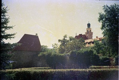 Vintage sepia-toned photo of a European village with a mix of rustic and historic architecture. A red-roofed cottage with sto...