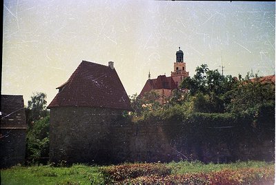 Vintage photograph of a European countryside scene featuring a rustic stone building with a steep red-tiled roof and chimney,...