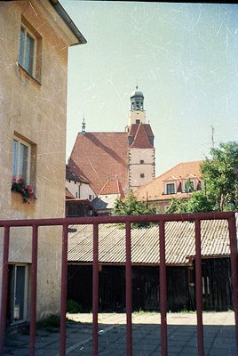 Historic European courtyard framed by rusted metal railings, showcasing a mix of stone and brick architecture. Prominent red-...