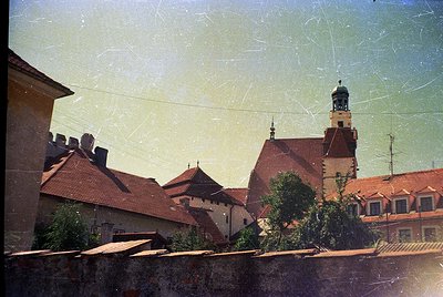 Vintage photograph of European medieval rooftops with aged sepia-toned filter. Distinctive red-tiled gables, a central tower ...