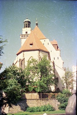 Historic castle with Gothic Revival architecture featuring a central tower and red-tiled roof, surrounded by lush greenery. L...