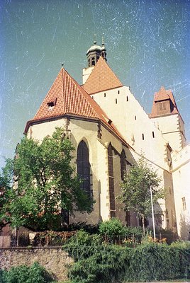 Historic church with Gothic Revival architecture—red-tiled conical roofs, pointed towers, and arched windows. Stone facade sh...