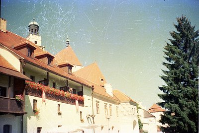 Vintage European street scene featuring a row of pastel-colored buildings with gabled roofs and flower boxes. A church tower ...