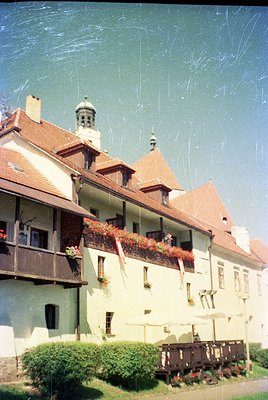 Vintage European-style building with gabled roofs, wooden balconies, and flower boxes. Central tower with a dome and cross su...
