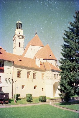 Historic castle complex featuring Gothic Revival architecture with a prominent tower and arched entrance. Stone walls, red-ti...