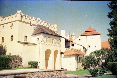Medieval-style castle complex with crenellated towers and stone walls, featuring a mix of red-tiled and slate roofs. Central ...