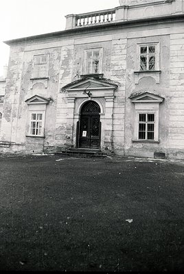 Neoclassical stone façade featuring a central arched doorway with wrought-iron gates, flanked by symmetrical rectangular wind...