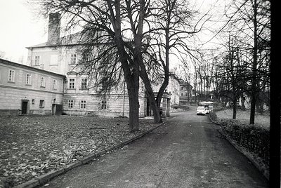 Black-and-white street scene featuring a grand, multi-story building with classical architectural elements—symmetrical window...