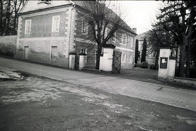Two-story institutional building with stone façade and wrought-iron gates, likely mid-20th century. Courtyard entrance flanke...