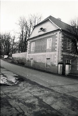 Two-story brick building with gabled roof, featuring a decorative stone cornice and a small relief sculpture near the rooflin...