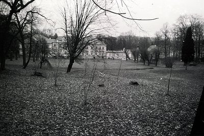 Black-and-white shot of a grand, multi-story building surrounded by a winter park. Symmetrical architecture with large window...