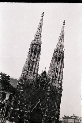 Gothic twin spires with intricate stone tracery and pointed arches dominate this mid-20th century cathedral facade. Ornate ro...
