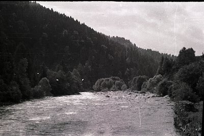 Black-and-white river scene with dense forest on both banks, flowing through a valley. Distinctive rocky outcrops and shallow...