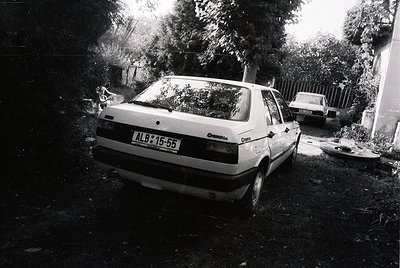 Vintage Opel Corsa parked in a residential driveway, license plate "ALB 15-55" suggests Albanian registration. Black-and-whit...