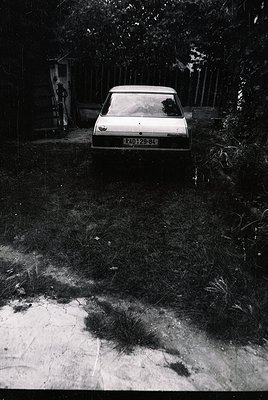 Vintage sedan parked on unpaved driveway beside overgrown foliage; license plate "RD 25-84" suggests Eastern Bloc-era vehicle...