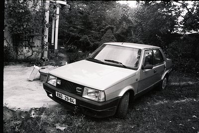 Vintage sedan (likely Škoda 130/136) parked on overgrown concrete, license plate "ВАД 29-84" suggests Bulgarian registration....