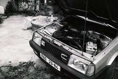 Vintage sedan with open hood revealing classic inline engine, likely a Škoda from the 1970s–80s. Rust and wear suggest long-t...