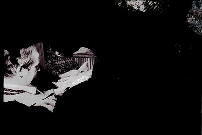 Low-contrast black-and-white photo of a seated figure in a dimly lit, classical-style interior. The person appears to be read...