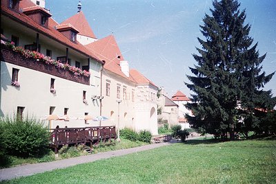 Vintage European courtyard with cream-colored building featuring red-tiled gables, wrought-iron balconies, and blooming flowe...