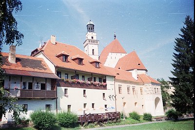 Historic European castle complex with red-tiled roofs and white plaster walls, featuring a central tower with crenellations. ...