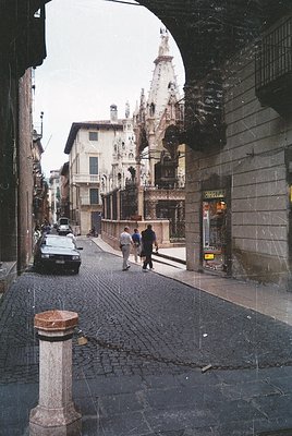 Historic European street scene under a stone archway, likely (). Cobblestone pavement, vintage car, and Gothic-style building...