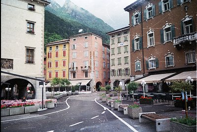 Alpine village square with multi-story buildings showcasing European alpine architecture—pastel facades, shuttered windows, a...