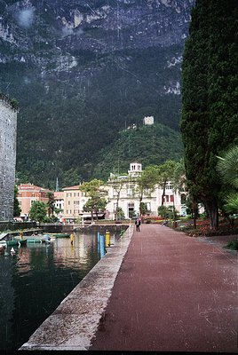 Lakefront promenade flanked by historic lakeside buildings in a European alpine town. Stone-paved walkway with wet reflection...