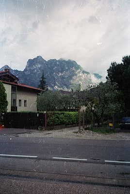 Vintage alpine town scene with misty peaks in background, likely Dolomites or Swiss Alps. Wet pavement reflects muted colors ...