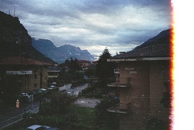 Vintage alpine village scene with "Villa Irma" signage, framed by aged photo borders. Snow-capped peaks loom under stormy ski...