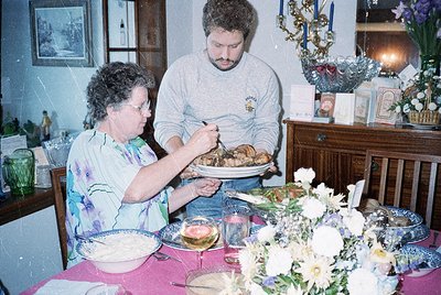 Vintage indoor family meal scene: woman and man serving roasted chicken at a floral-decorated table with vintage dishes. Wood...