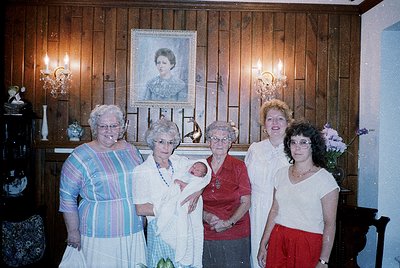 Family portrait featuring five women in a rustic interior, likely 1980s–1990s. Central figure holds a newborn, surrounded by ...