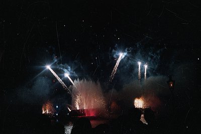 Fireworks display illuminating night sky with starbursts and cascading trails. Silhouetted figures below suggest crowd celebr...