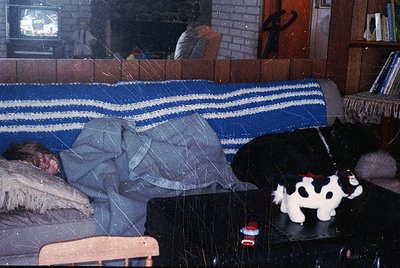 Vintage living room scene with a child sleeping on a striped blanket-covered sofa, surrounded by retro decor. A black-and-whi...